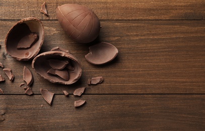 Photo of Broken chocolate eggs on wooden table, flat lay. Space for text