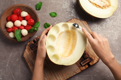 Woman making melon balls at table, top view