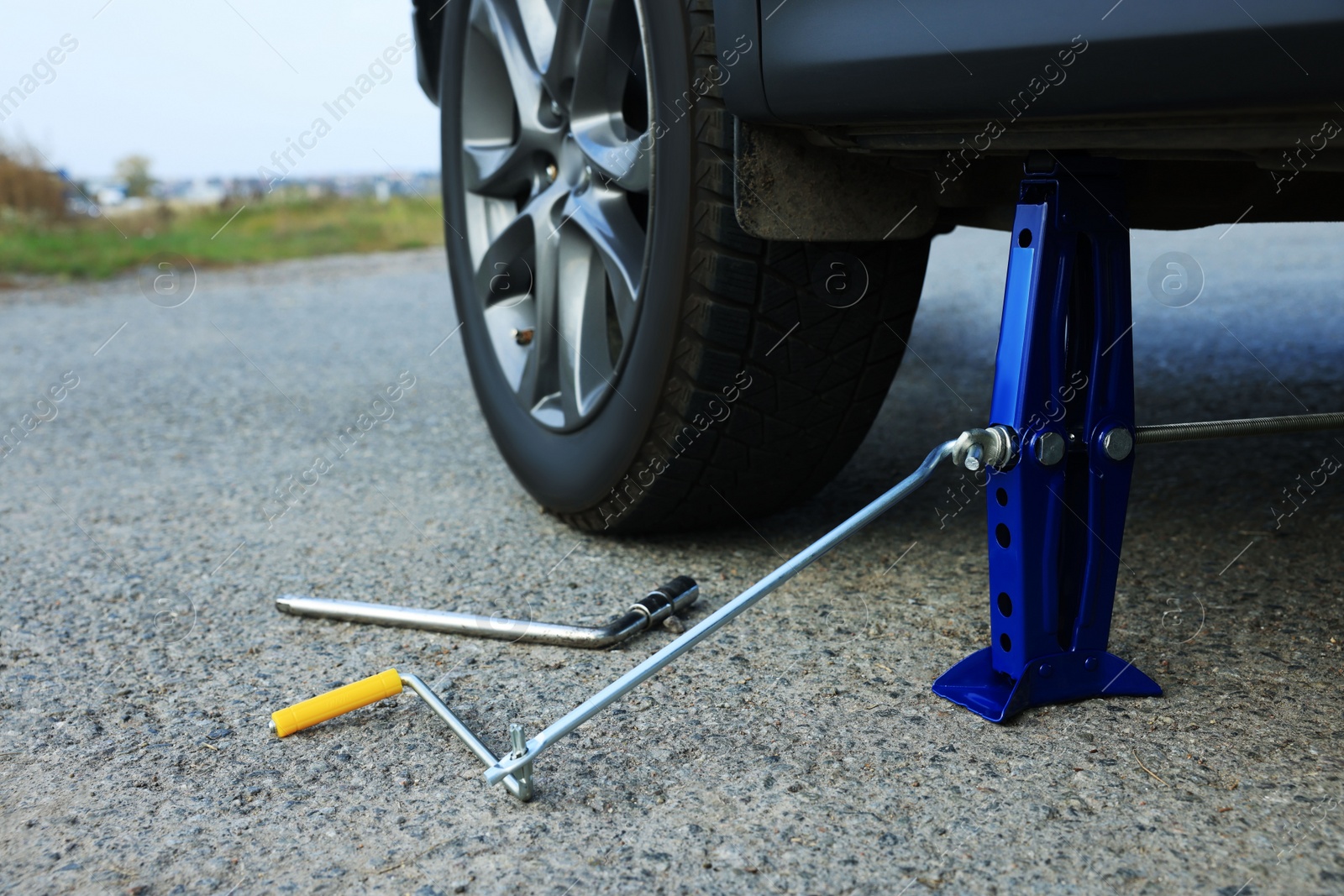 Photo of Car lifted by scissor jack without wheel outdoors, closeup. Tire puncture