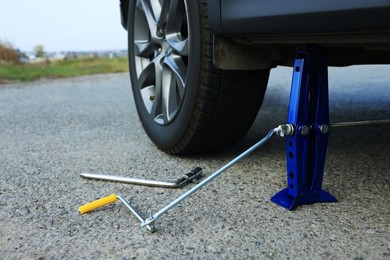 Photo of Car lifted by scissor jack without wheel outdoors, closeup. Tire puncture