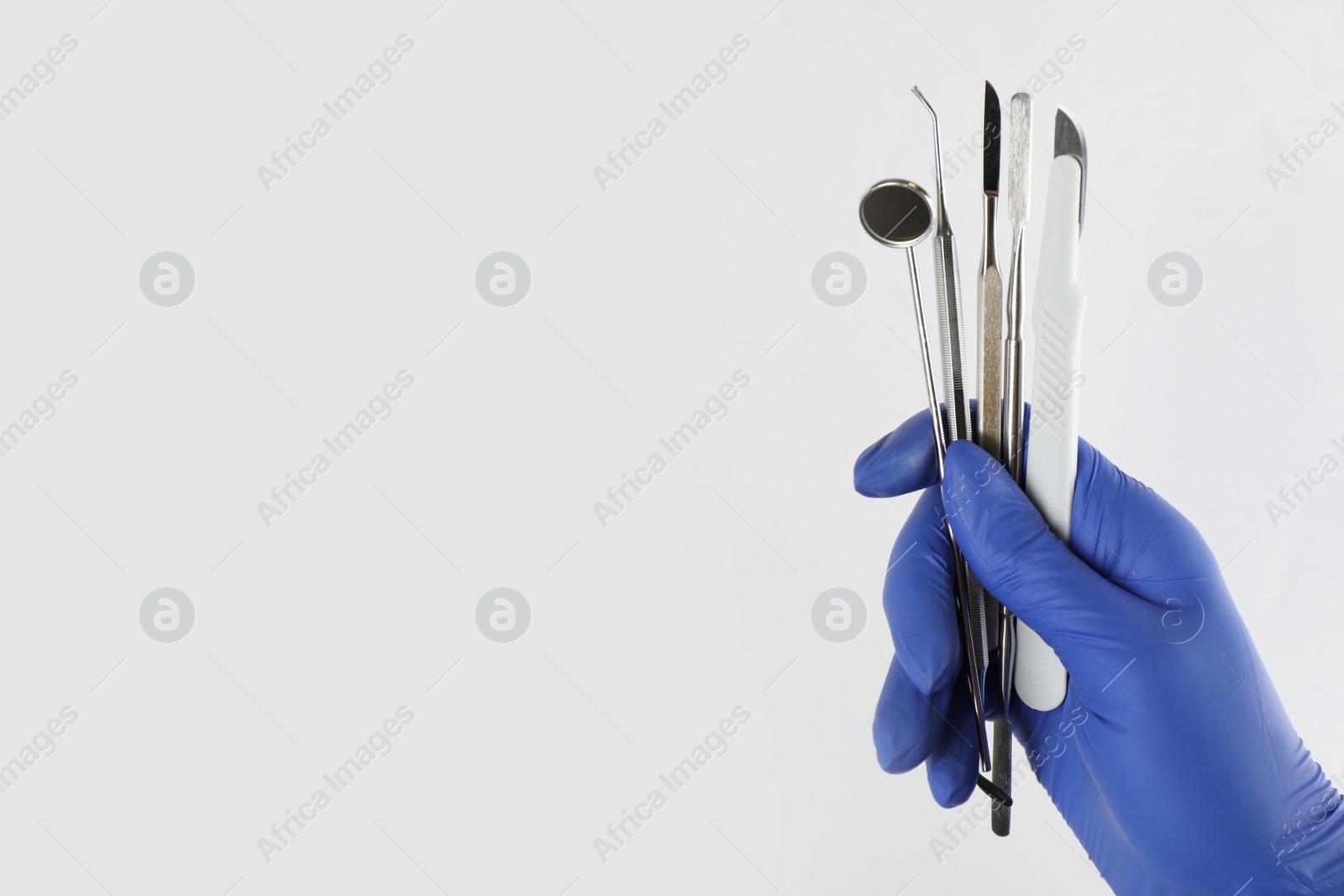 Photo of Dentist holding set of tools on light background, closeup. Space for text