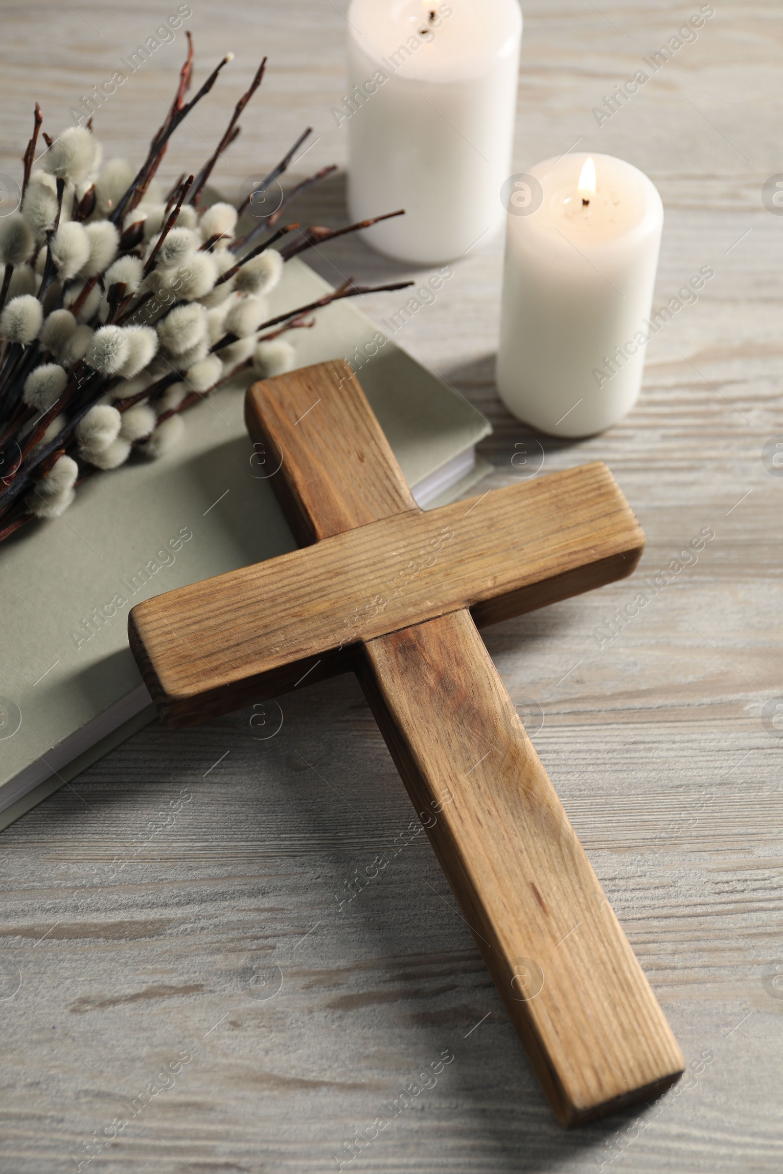 Photo of Burning candles, cross, book and willow branches on wooden table