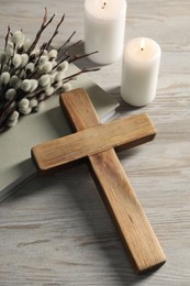 Burning candles, cross, book and willow branches on wooden table