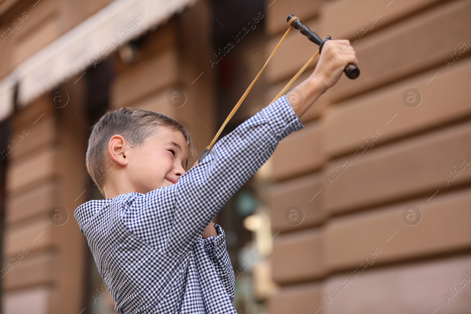 Photo of Little boy playing with slingshot outdoors on city street