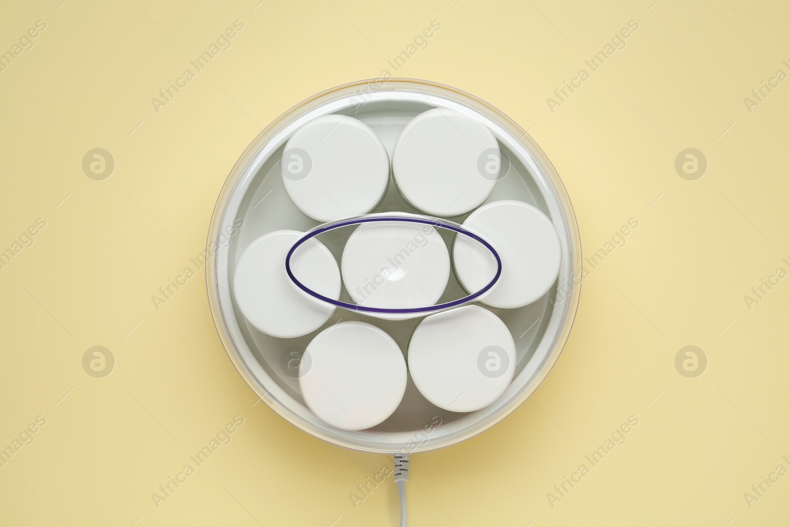 Photo of Modern yogurt maker with jars on beige background, top view