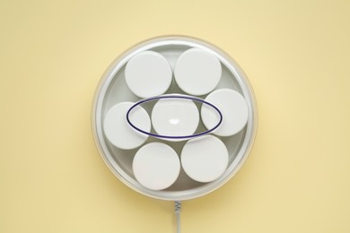 Modern yogurt maker with jars on beige background, top view