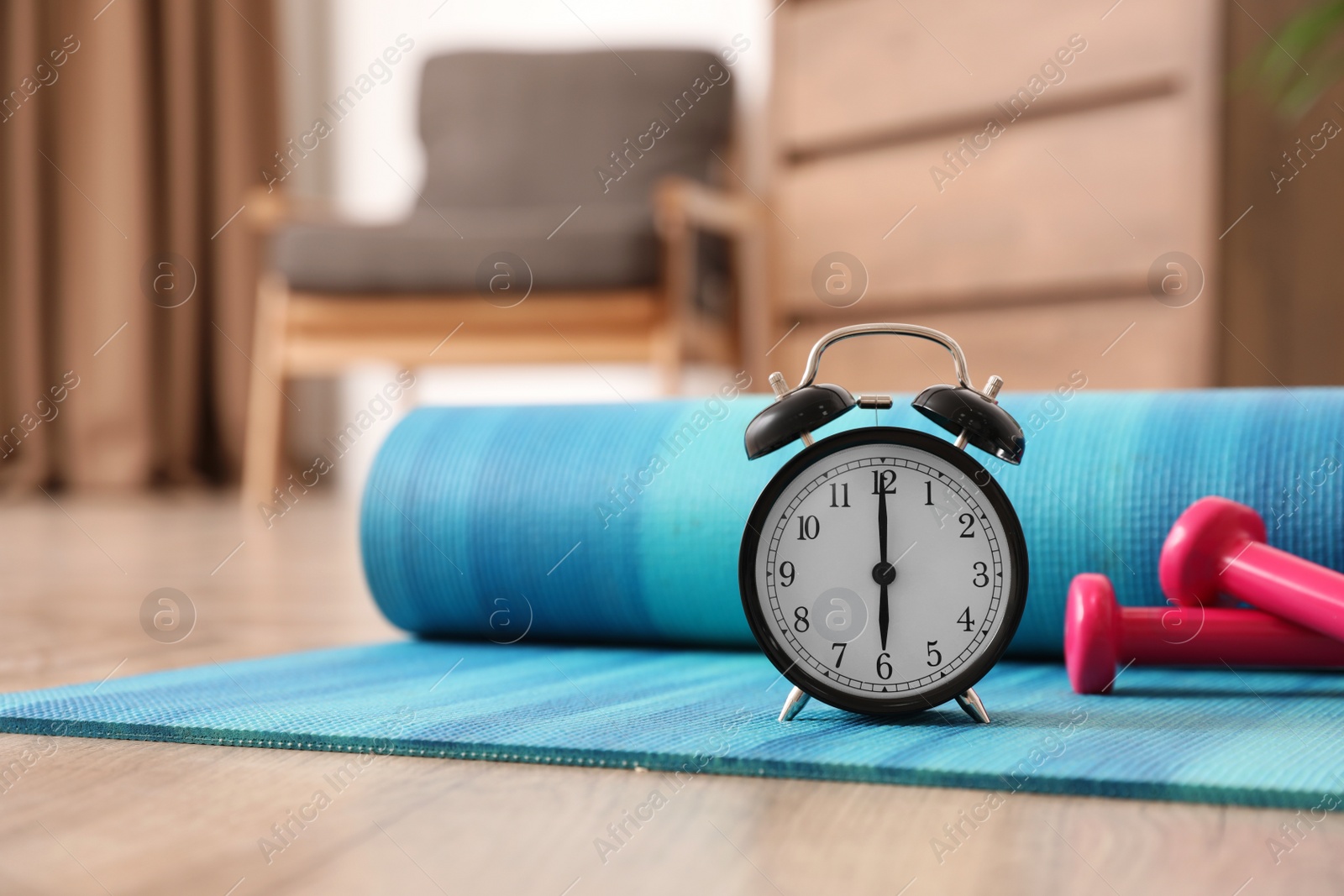 Photo of Alarm clock, yoga mat and dumbbells on wooden floor indoors. Morning exercise