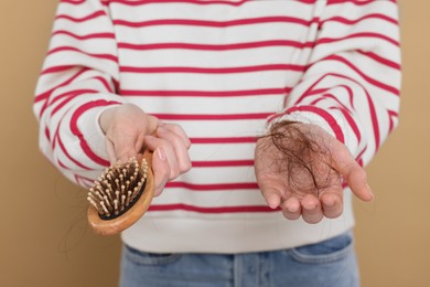 Photo of Woman holding brush with lost hair on beige background, closeup. Alopecia problem