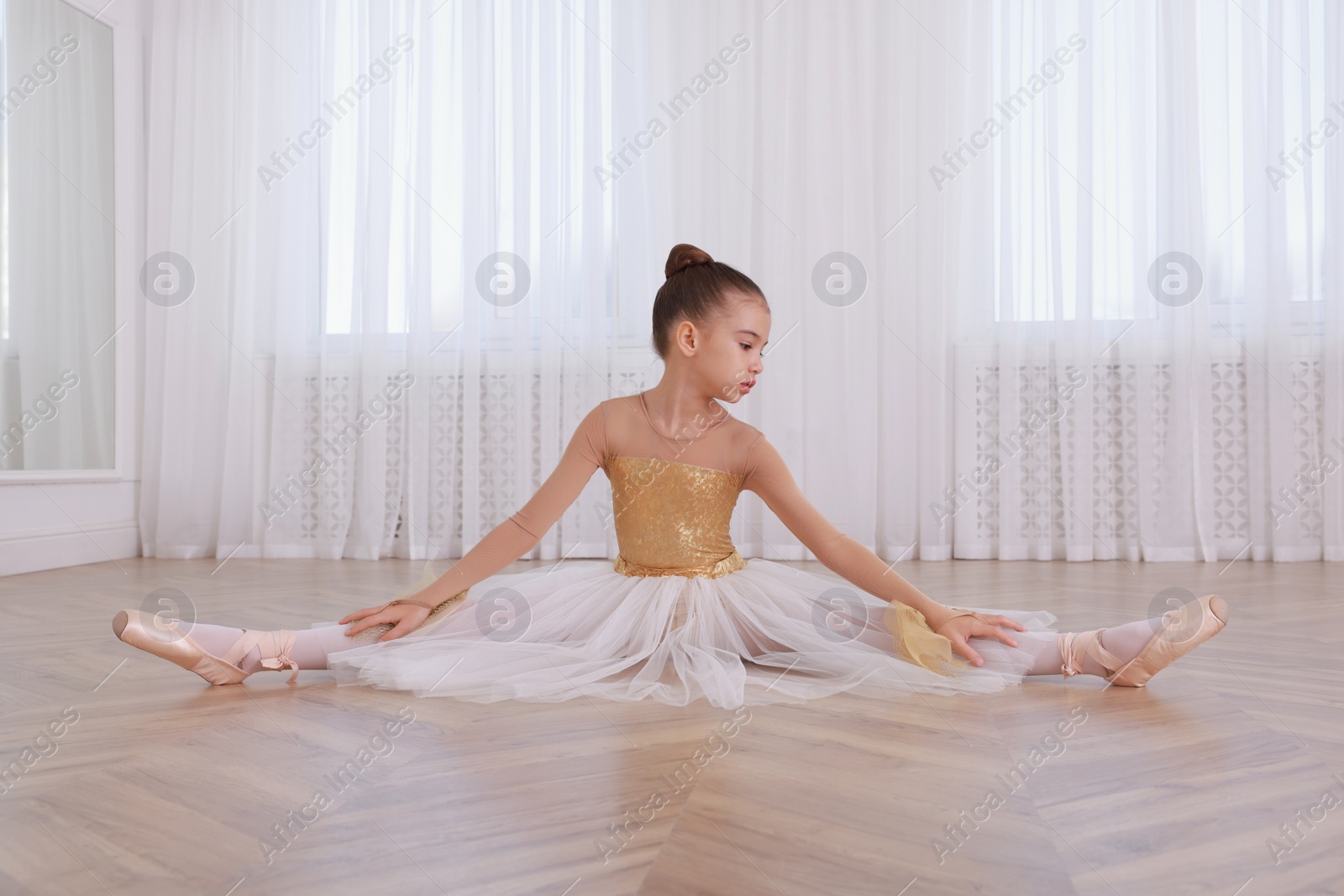 Photo of Beautifully dressed little ballerina stretching in studio