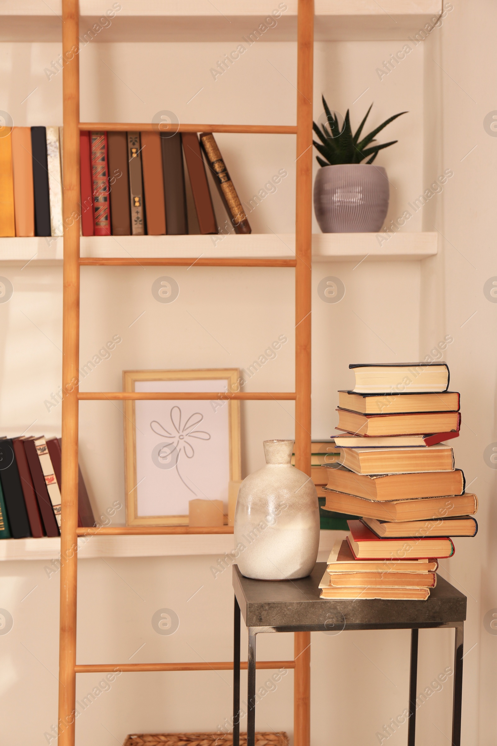 Photo of Stack of different books and vase on table near bookshelves in home library