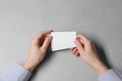 Photo of Woman holding blank cards at light grey table, top view. Mockup for design