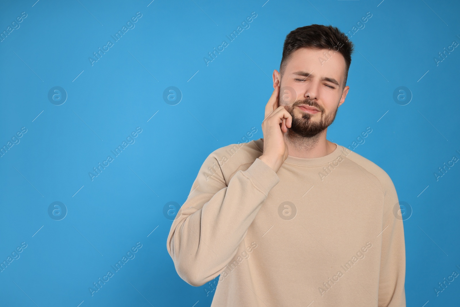 Photo of Young man suffering from ear pain on light blue background. Space for text