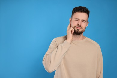 Young man suffering from ear pain on light blue background. Space for text