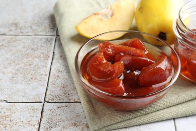 Tasty homemade quince jam in bowl and fruits on tiled table, closeup. Space for text