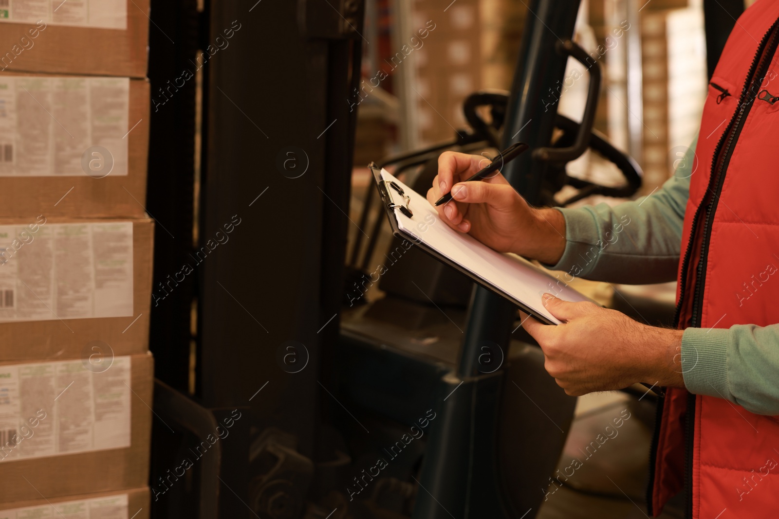Image of Worker near forklift truck with cardboard boxes in warehouse, closeup. Logistics concept
