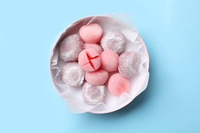 Photo of Many different delicious mochi in box on light blue background, top view. Traditional Japanese dessert