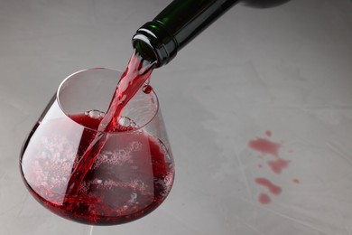 Photo of Pouring tasty red wine in glass at gray table, closeup. Space for text