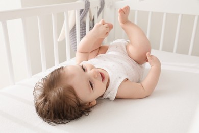 Photo of Cute little baby lying in comfortable crib at home