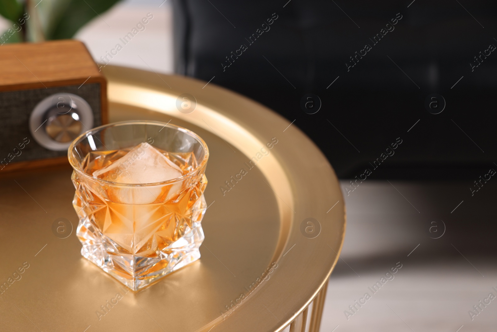 Photo of Alcohol drink with ice cube on golden table in room, space for text. Relax at home