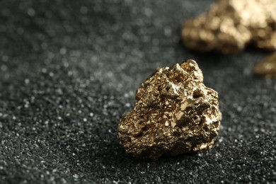 Photo of Shiny gold nugget on black sand, closeup. Space for text
