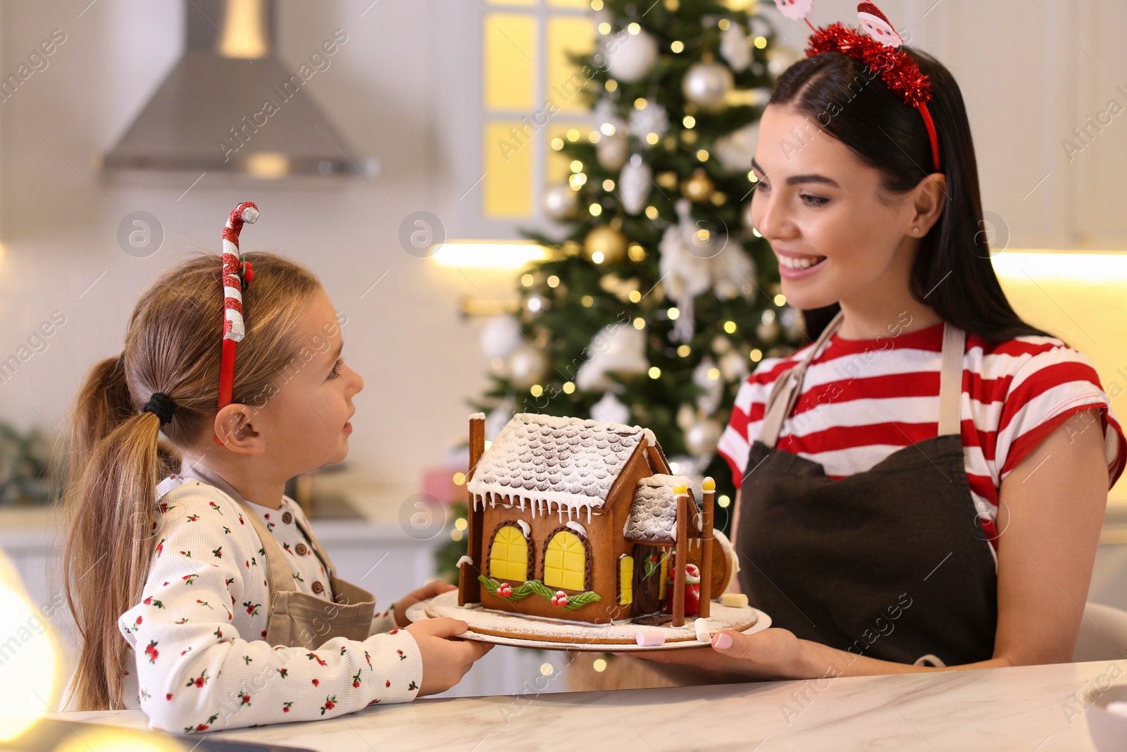 Photo of Mother and daughter with gingerbread house in kitchen