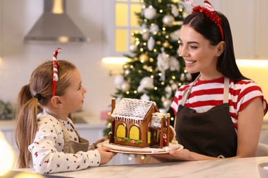 Mother and daughter with gingerbread house in kitchen