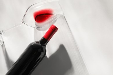 Photo of Bottle of expensive red wine and wineglass on light background, top view. Space for text
