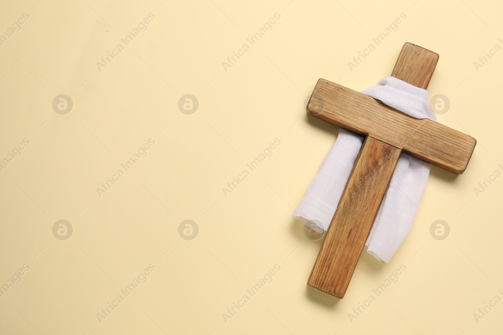 Photo of Wooden cross and white cloth on beige background, top view with space for text. Easter attributes