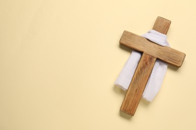 Photo of Wooden cross and white cloth on beige background, top view with space for text. Easter attributes