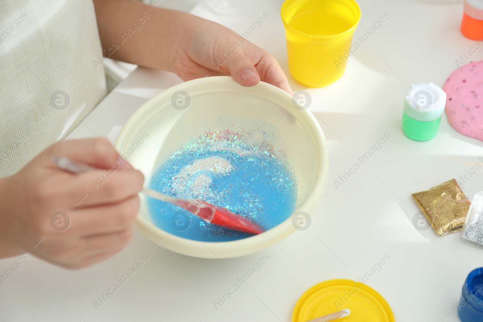 Photo of Little girl mixing ingredients with silicone spatula at table, closeup. DIY slime toy