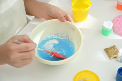 Photo of Little girl mixing ingredients with silicone spatula at table, closeup. DIY slime toy