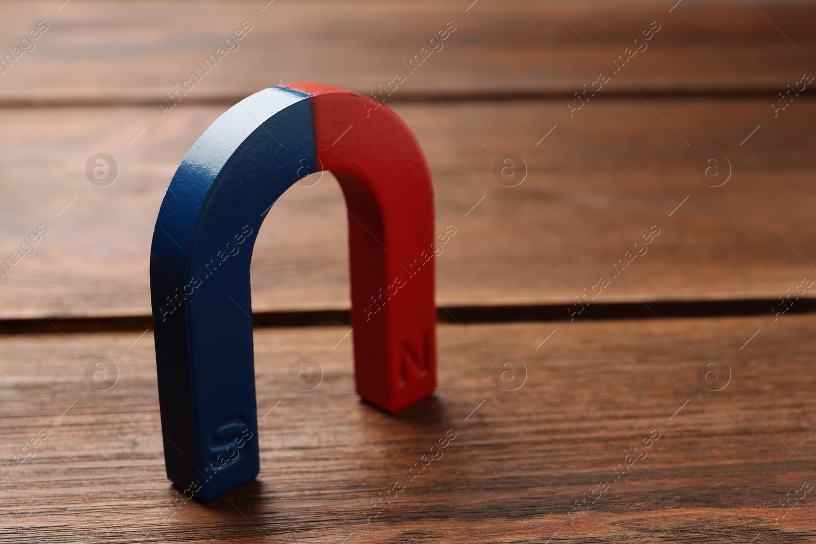 Photo of Red and blue horseshoe magnet on wooden background. Space for text
