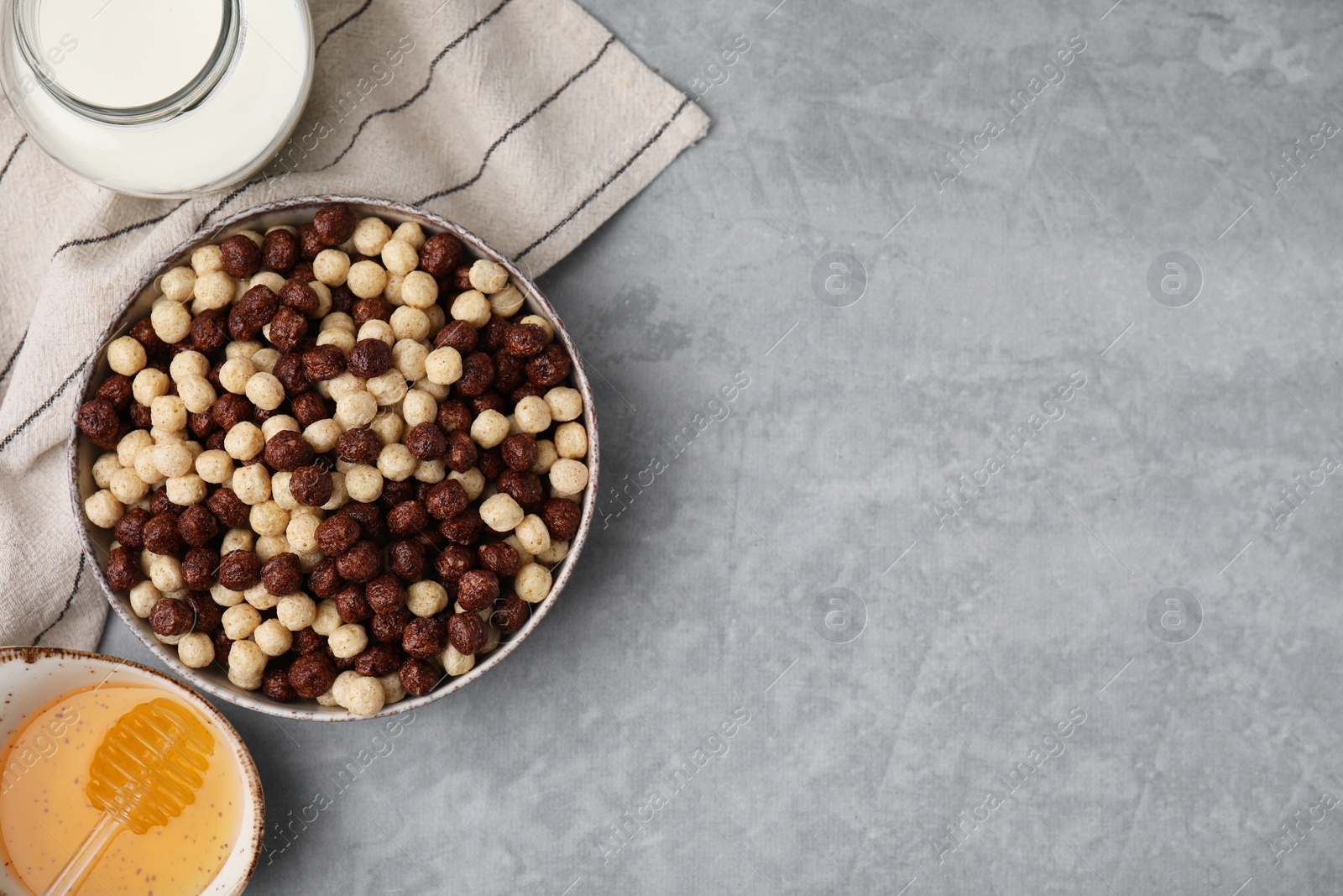 Photo of Tasty cereal balls in bowl, milk and honey on grey table, flat lay. Space for text