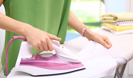 Young woman ironing clean laundry indoors, closeup. Space for text