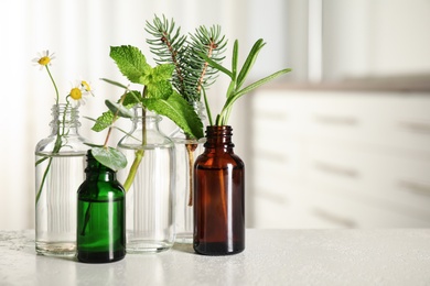 Glass bottles of different essential oils with plants on table. Space for text