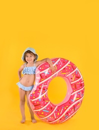 Photo of Cute little child in beachwear with bright inflatable ring on yellow background