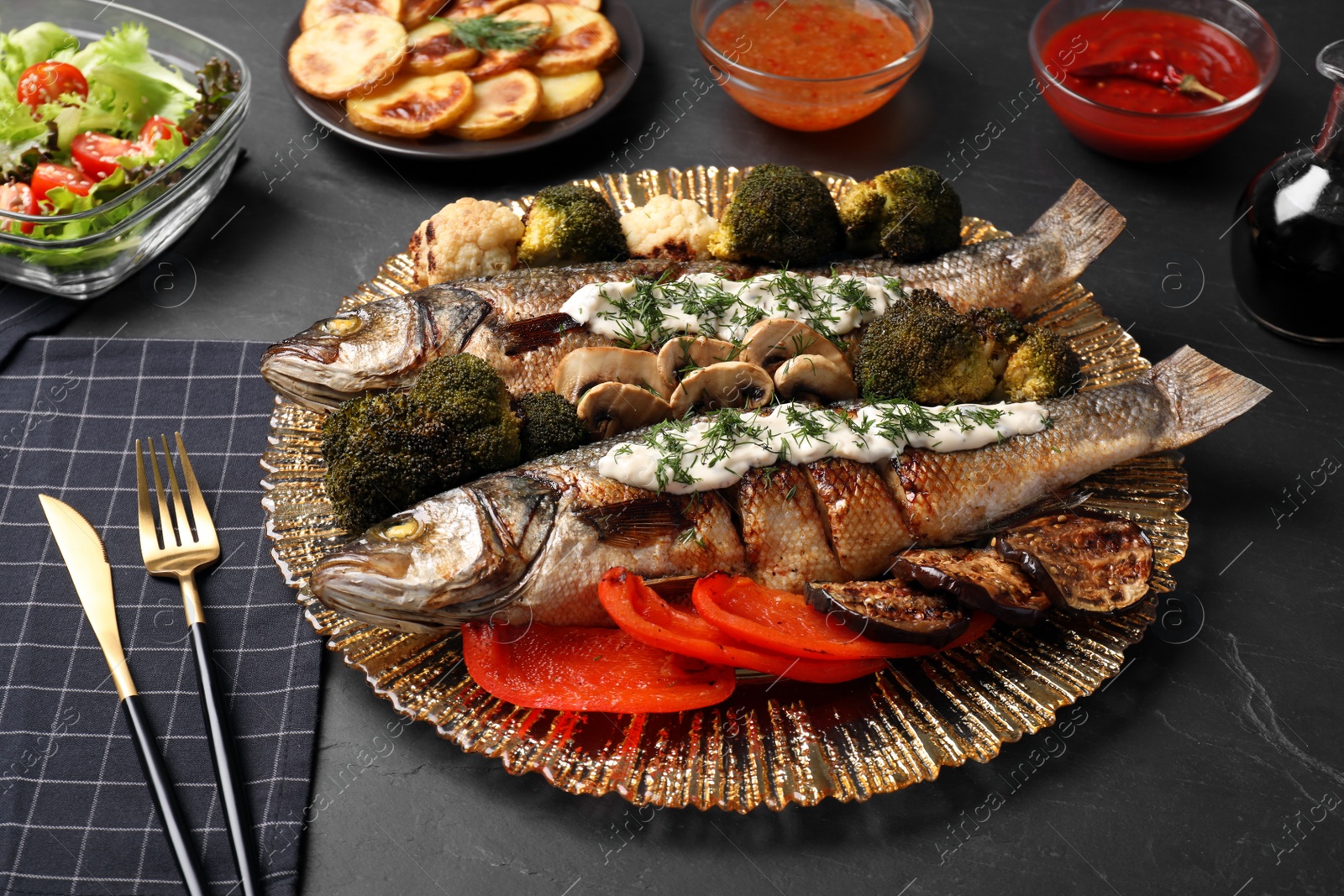 Photo of Plate with delicious baked sea bass fish and sauce served on dark table