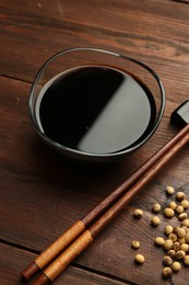 Photo of Soy sauce in bowl, soybeans and chopsticks on wooden table