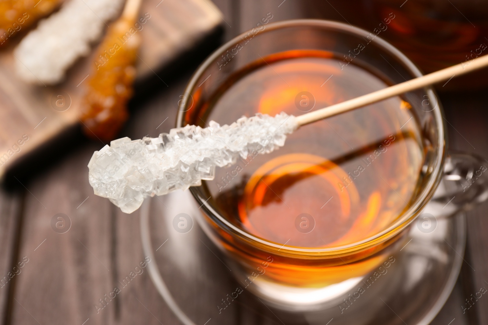 Photo of Stick with sugar crystals and cup of tea on wooden table, closeup