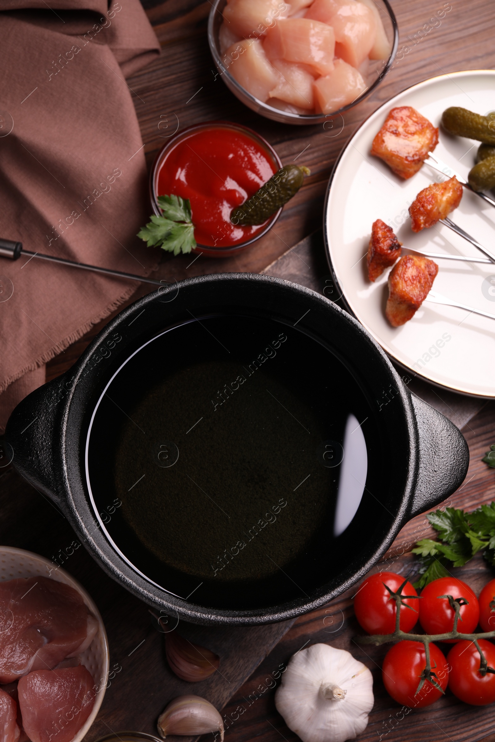 Photo of Fondue pot, forks with fried meat pieces and other products on wooden table, flat lay