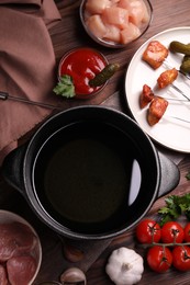 Fondue pot, forks with fried meat pieces and other products on wooden table, flat lay