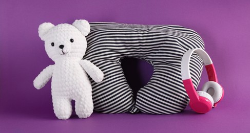 Photo of Striped travel pillow, toy bear and headphones on violet background