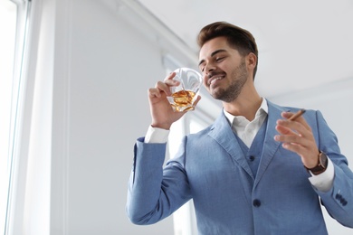 Man with glass of whiskey and cigar indoors