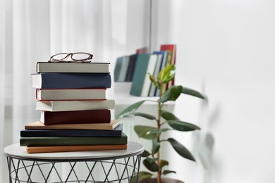 Stack of many different books and glasses on coffee table indoors. Space for text