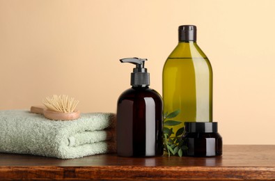 Photo of Bottles of shampoo, hairbrush and stacked towel on wooden table near beige wall