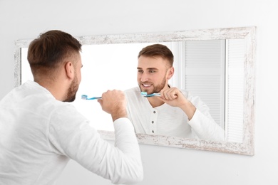 Photo of Young man cleaning teeth against mirror in bathroom