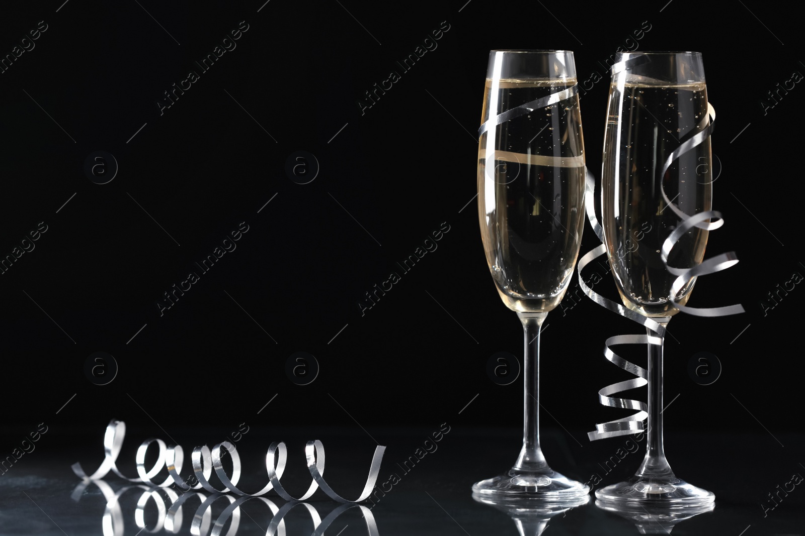 Photo of Glasses of champagne and serpentine streamers on black background. Space for text