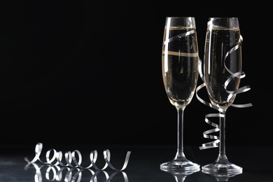 Glasses of champagne and serpentine streamers on black background. Space for text