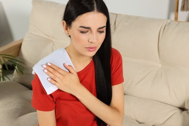 Photo of Young woman using heating pad at home
