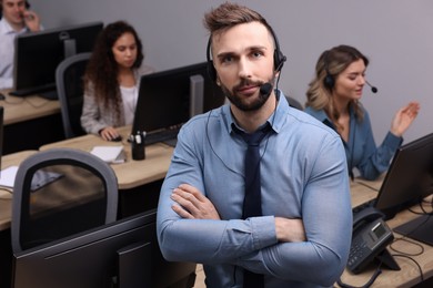 Photo of Handsome call center operator with headset and his colleagues working in modern office